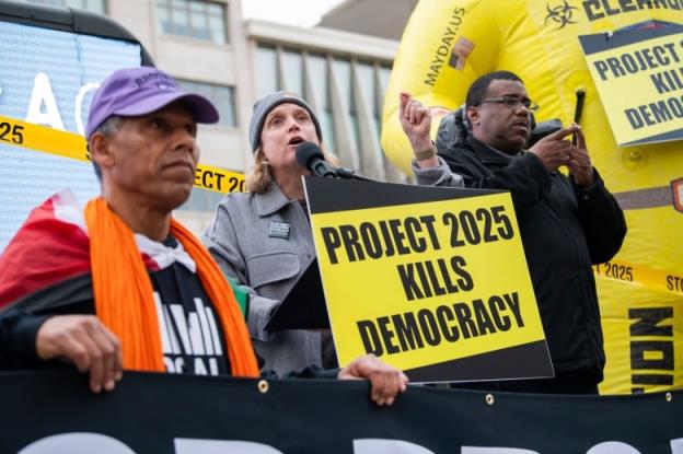 A man holds a yellow and black protest sign reading 