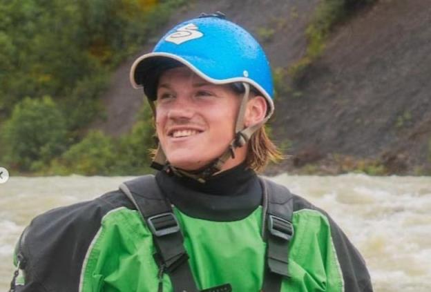 A man wearing a blue helmet and a green life-preserver sits in a kayak.