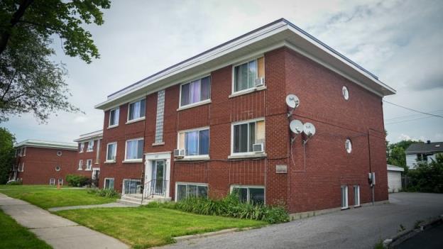 A square red-brick apartment building with twelve windows across the front. 