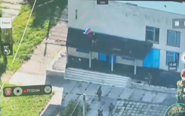 Soldiers are seen outside a building in a grainy photograph. One man is on the roof holding a flag. 