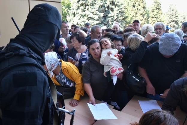 A crowd of people push against a table when a soldier hands out papers.