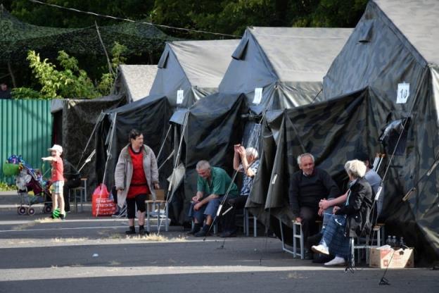 People sit outside a row of tents.